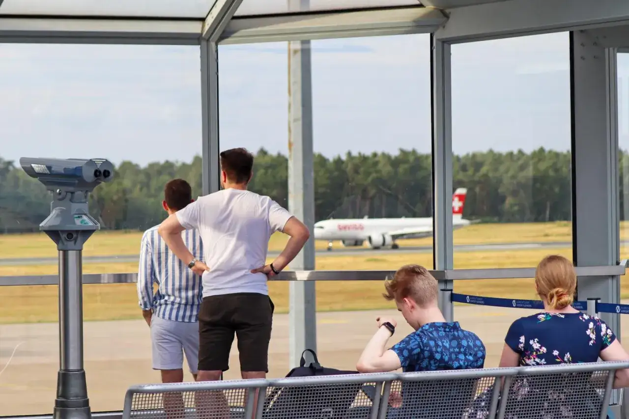 Menschen warten am Flughafen und beobachten ein Flugzeug. Einer der Männer freut sich aufs Flugzeuge fotografieren.