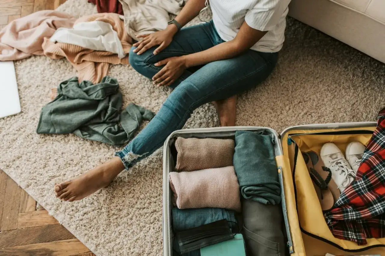 Packliste Wellnessurlaub: Kleidung wird für eine Reise zusammengelegt. Ein Koffer ist bereits gepackt mit Pullovern, Hosen und Schuhen.