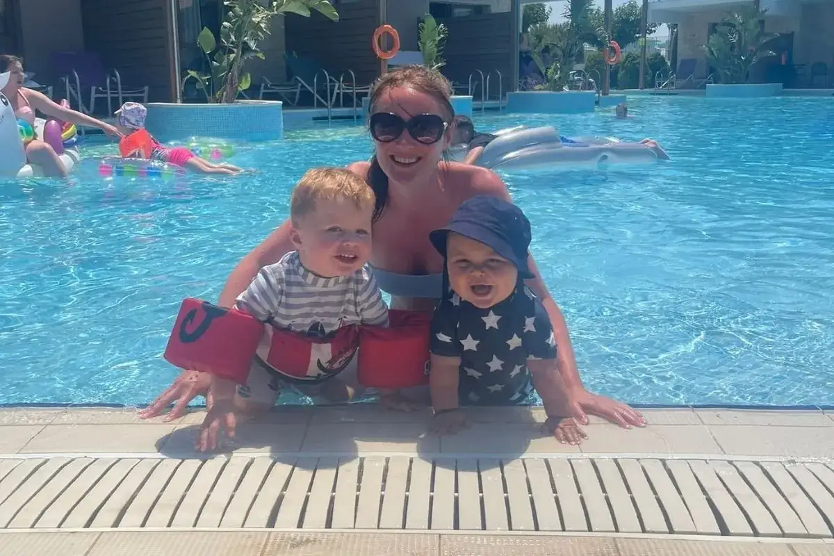 Gl&uuml;ckliche Familie im Pool, ein magischer TUI Magic Life Plimmiri Urlaub. Zwei kleine Kinder mit Schwimmfl&uuml;geln und eine Frau genie&szlig;en das Wasser.