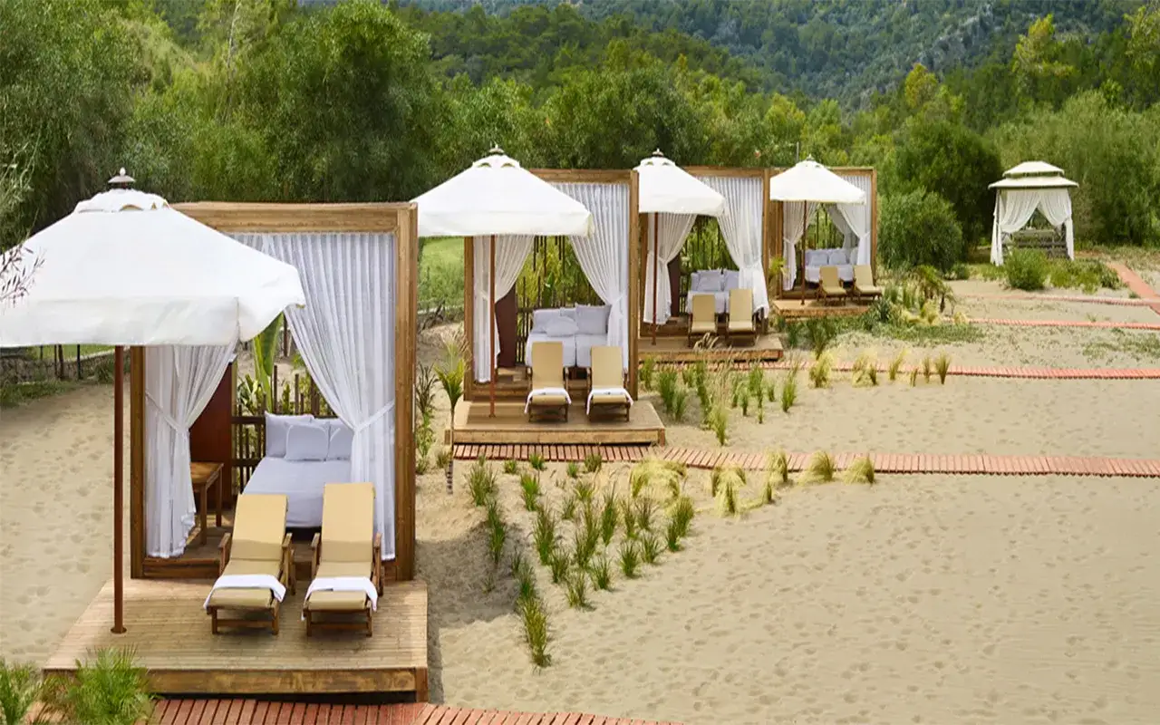 Entspannende Strandpavillons im TUI Blue Sarigerme Park mit Liegen und Betten, umgeben von Sand und üppiger Vegetation.