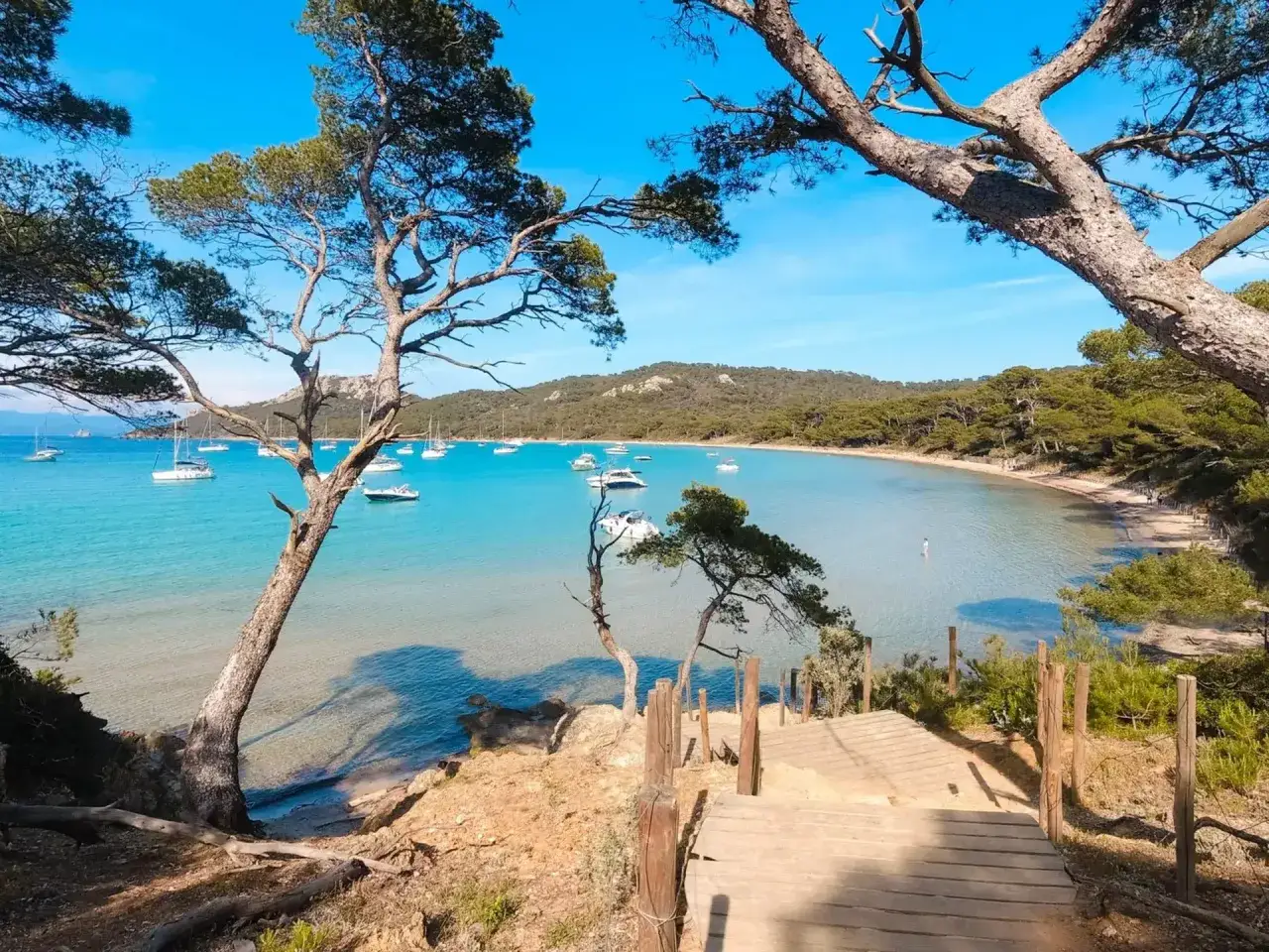Traumhafte Bucht mit Segelbooten, ideal für Urlaubsziele in Europa. Holztreppe führt zum türkisfarbenen Wasser.
