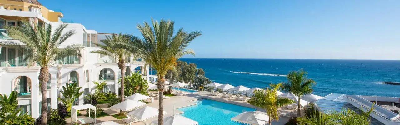 Traumhafter Blick vom Riu Palace Teneriffa auf den blauen Ozean, Palmen und einen Pool.