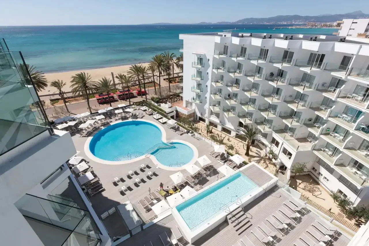 Ein modernes Hotel mit Pools und Liegestühlen am Strand. Palmen und das türkisfarbene Meer schaffen eine hm tropical Atmosphäre.