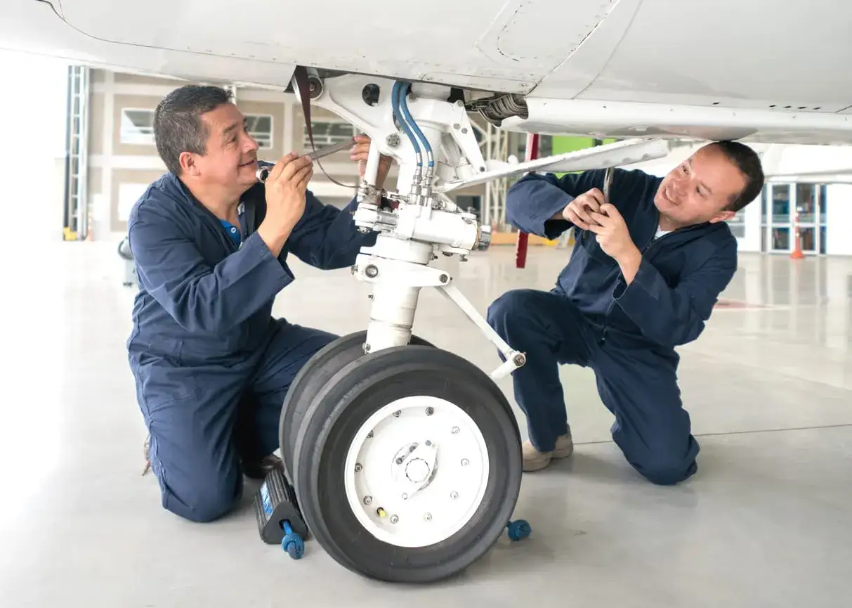 Zwei Mechaniker prüfen das Fahrwerk eines Flugzeugs. Ihre Arbeit ist entscheidend für die Sicherheit von Fluggesellschaften.