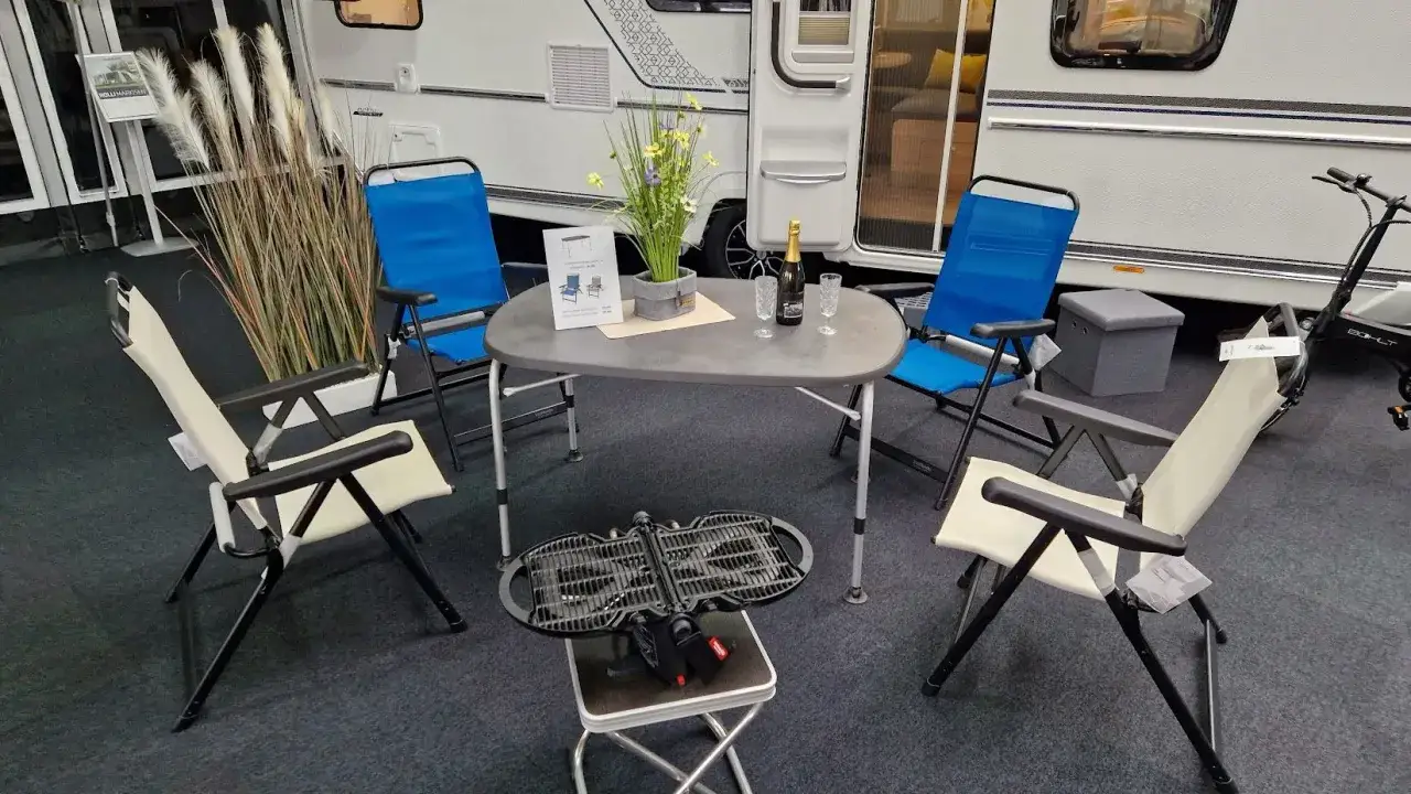 Gemütliche Camping-Ecke vor einem Wohnwagen: Tisch, Stühle, Grill und Deko. Perfekt für die Wohnwagen-Checkliste!