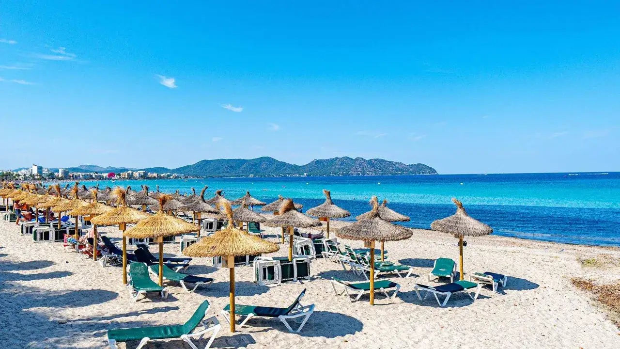 Sonnige Bucht Cala Millor mit vielen Liegestühlen und Strohschirmen am türkisfarbenen Meer.