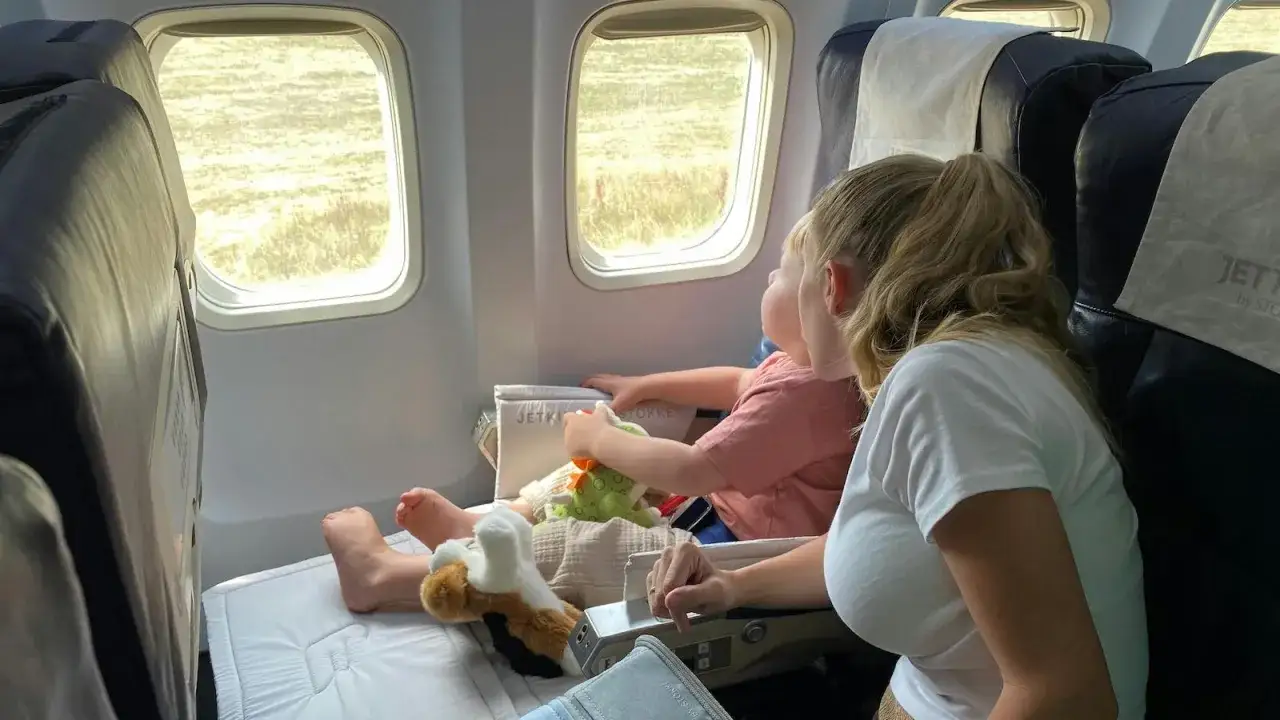 Mutter und Kind genießen den besten Sitzplatz im Flugzeug mit Kleinkind. Das Kind schaut aus dem Fenster, während es mit Spielzeug spielt.