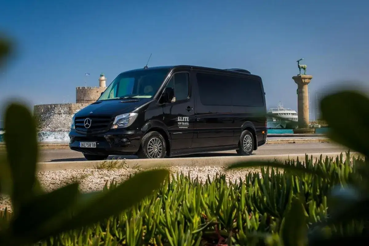 Schwarzer VIP-Van von Elite VIP Travel am Flughafen Rhodos, mit Blick auf das Meer und die historische Festung.