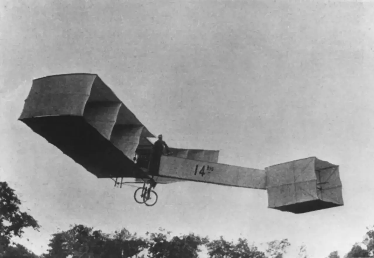 Ein Mann fliegt in einem frühen Flugzeug, das an ein Fahrrad erinnert. Dies zeigt, seit wann es Flugzeuge gibt und wie sie sich entwickelten.