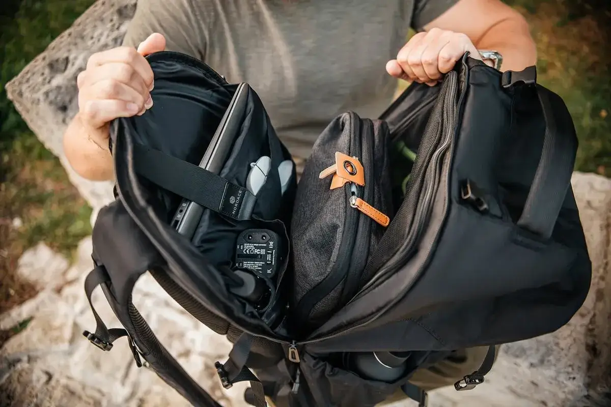 Person packt einen Rucksack platzsparend: Laptop, Brille, Adapter und eine Tasche sind ordentlich verstaut.