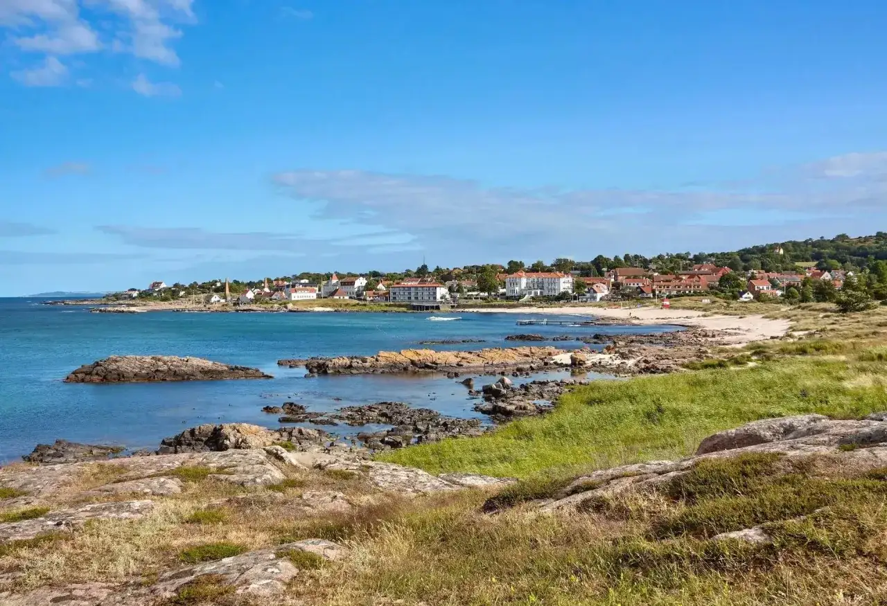 Idyllische Küstenlandschaft mit Felsen und Sandstrand. Ein malerisches Dorf mit roten Dächern lädt zum Urlaub auf Bornholm ein.