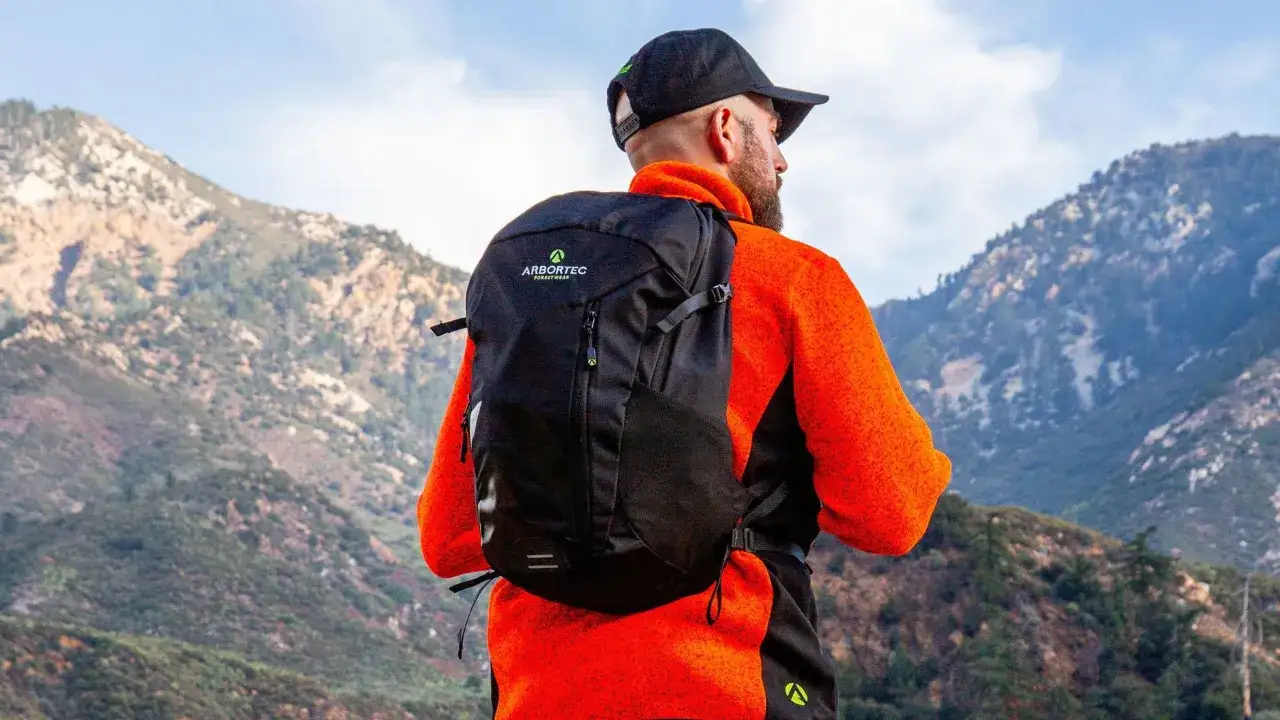 Mann mit Rucksack und orangefarbener Jacke blickt auf Berge. Perfekt für die Packliste Wanderurlaub.