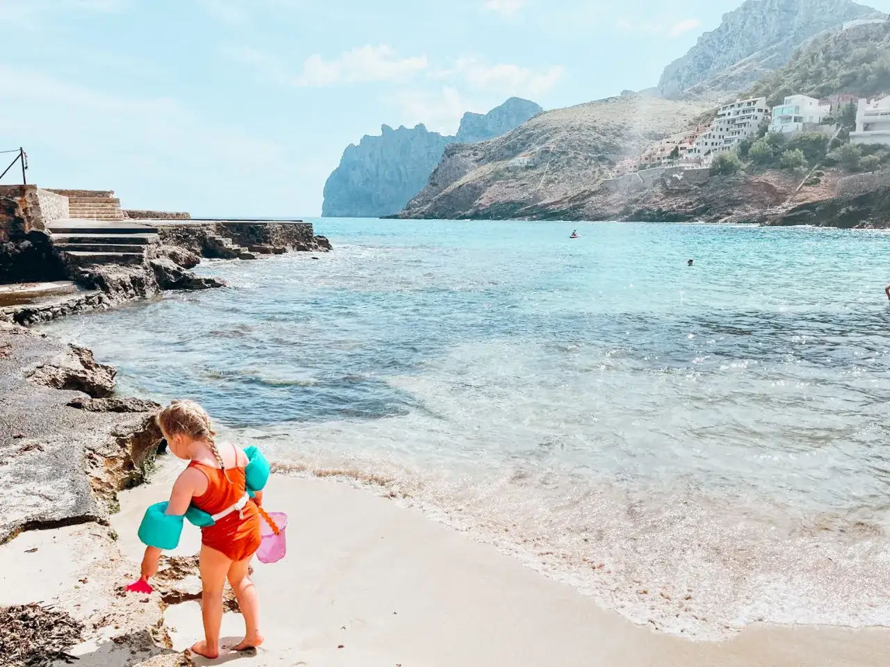 Kleines Mädchen mit Schwimmflügeln und Eimer am Strand. Perfekt für die Packliste Mallorca für einen sonnigen Urlaub.