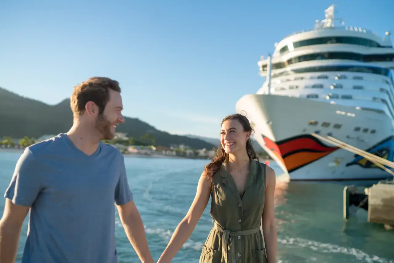Glückliches Paar hält Händchen vor AIDA Schiff. Perfekt für die Packliste Kreuzfahrt AIDA.