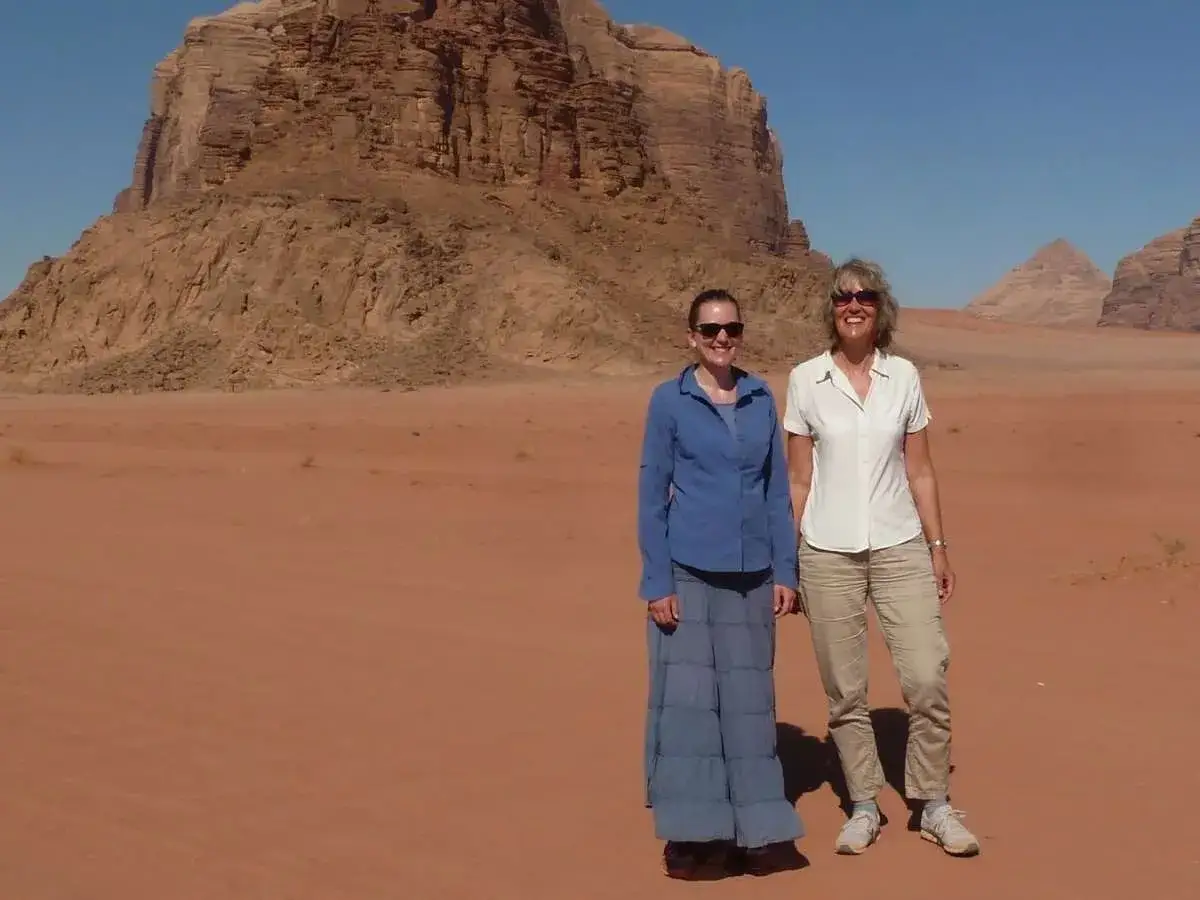 Zwei Frauen stehen in der Wüste Jordaniens vor beeindruckenden Felsen. Perfekt für die Packliste Jordanien: leichte Kleidung, Sonnenbrillen und bequeme Schuhe.
