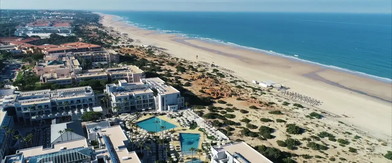 Luftaufnahme von Hipotels Barrosa Park mit Blick auf den Strand und das Meer. Mehrere Hotelgebäude mit Pools und Sonnenschirmen sind zu sehen.