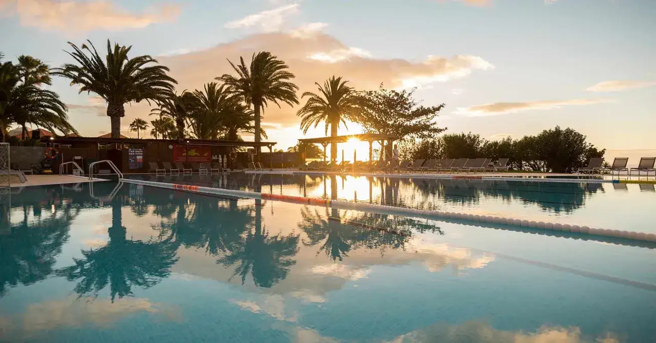 Sonnenuntergang am Robinson Esquinzo Playa. Palmen spiegeln sich im Pool.