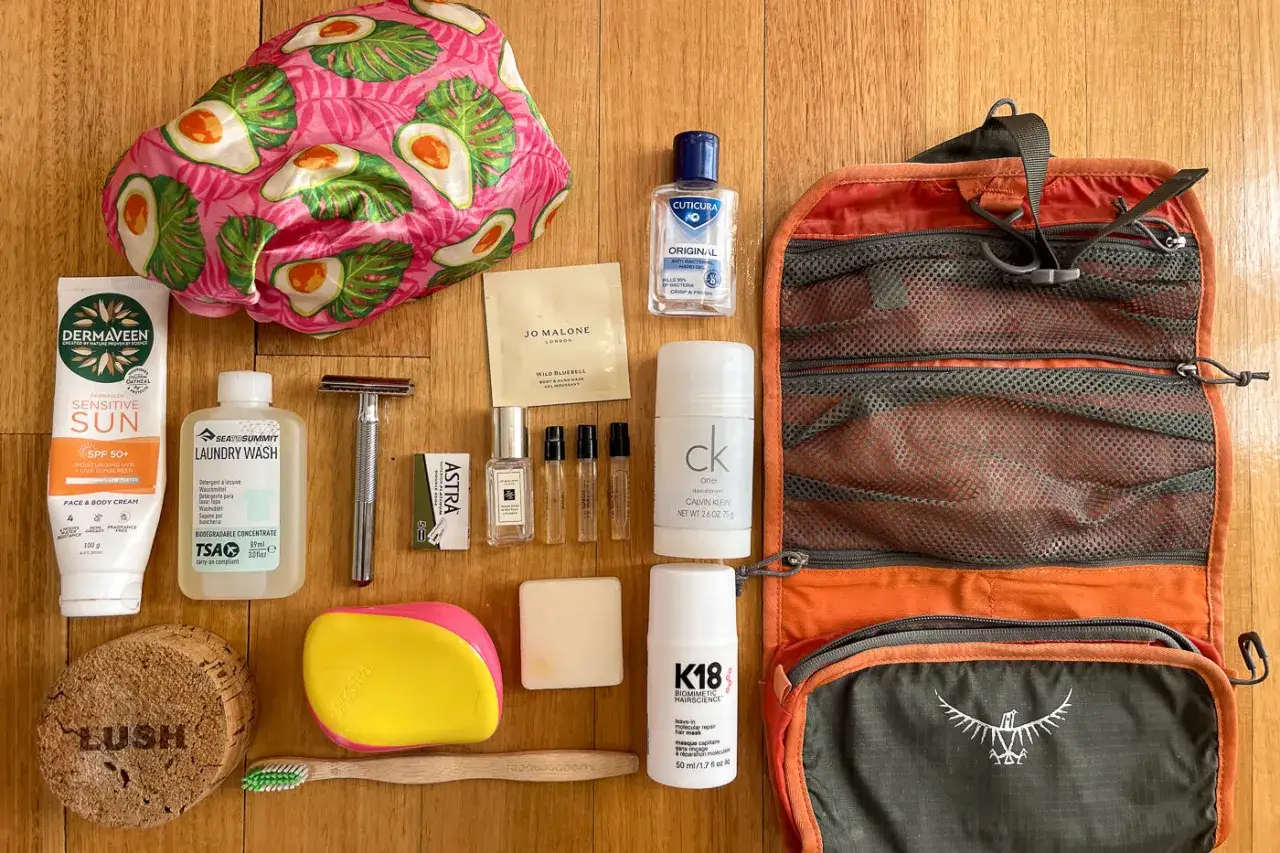 Packliste Kroatien: Sonnencreme, Rasierer, Waschmittel, Duschhaube mit Avocado-Print, Deo und weitere Reiseutensilien in einer Kulturtasche.