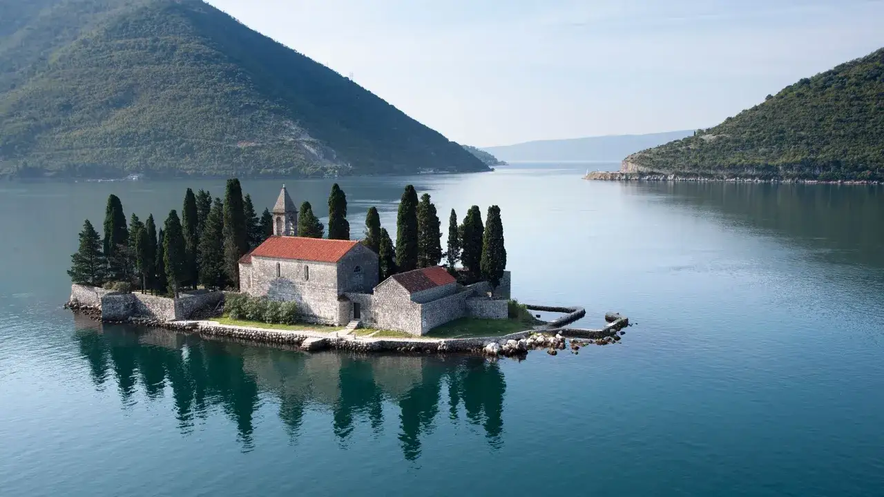 Kleine Insel mit Kirche und Zypressen im ruhigen Wasser, ein malerischer Ort f&uuml;r einen Urlaub in Montenegro.