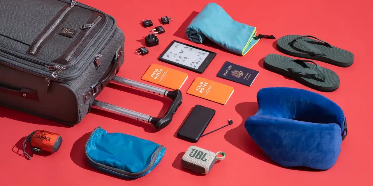 Koffer packen: Reiseutensilien wie Koffer, Reisepass, Kindle, Adapter, Nackenkissen und Flip-Flops liegen bereit.