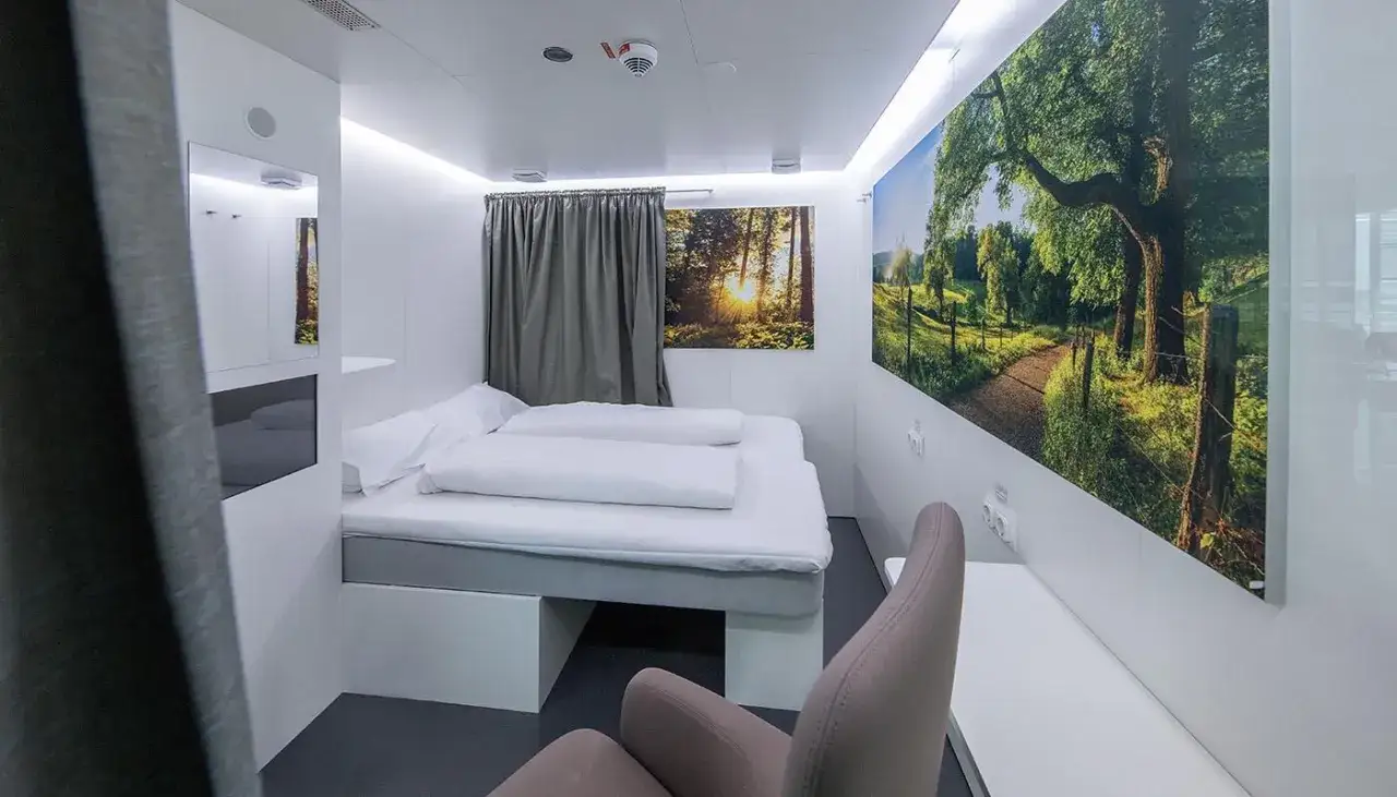 Gemütliches napcabs Zimmer am Münchner Flughafen mit Bett, Sessel und Naturmotiven.