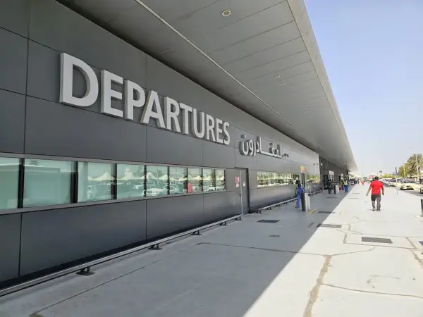 Große "DEPARTURES" Schriftzüge am Flughafen Dubai Terminal 3. Menschen und Autos spiegeln sich in den Fenstern.