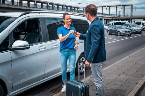 Mann übergibt Schlüssel an Frau neben weißem Van. Das bedeutet Valet-Service: bequemes Parken am Flughafen.