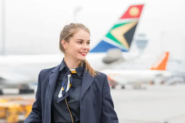 Lächelnde Stewardess am Flughafen vor Flugzeugen. Für einen Langstreckenflug sollte man mindestens 2 Stunden vorher am Flughafen sein.