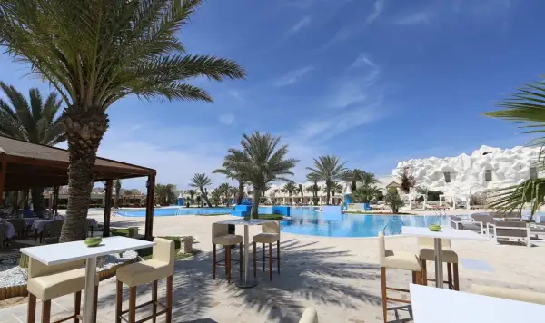 Sonnige Poolanlage mit Palmen und weißen Liegestühlen im Robinson Club Djerba.