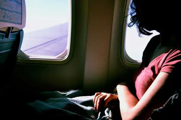 Frau mit extremer Flugangst blickt aus dem Flugzeugfenster. Die Flügel sind im violetten Licht zu sehen.