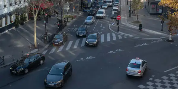 Verkehr in Paris: Autos und Taxis auf dem Weg zum Ziel. Ein silbernes Taxi fährt über den Zebrastreifen, während andere Fahrzeuge im Stau stehen.