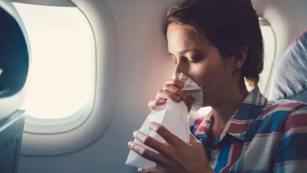 Frau mit Tüte gegen Reisekrankheit im Flugzeug.