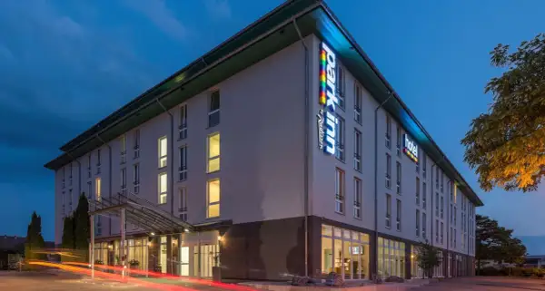 Das Park Inn Wien bei Nacht, beleuchtet mit bunten Lichtern. Autos fahren vorbei und hinterlassen rote Lichtspuren.