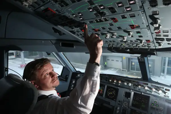 Pilot im Cockpit prüft die Anzeigen. Er bedient einen Schalter, während draußen Schnee liegt.