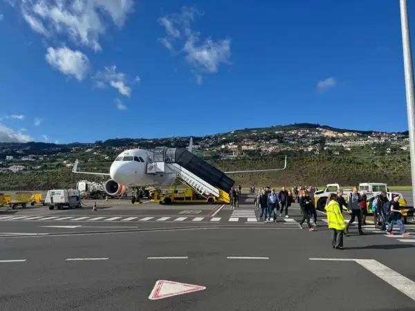Passagiere steigen am Madeira Flughafen aus dem Flugzeug. Im Hintergrund erstreckt sich eine hügelige Landschaft mit Häusern.