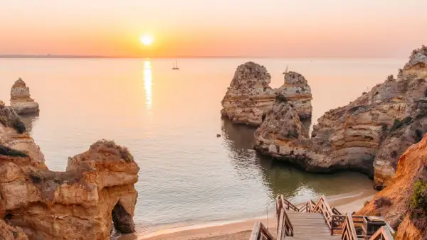 Sonnenuntergang an der Algarve: Ein perfekter Urlaub in Portugal am Meer mit Felsformationen und einer Holztreppe zum Strand.