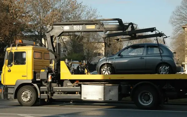 Gelber Abschleppwagen mit grauem Kleinwagen auf der Ladefläche. Ein unerwarteter Stopp, die abschleppkosten 400 euro sind ärgerlich.