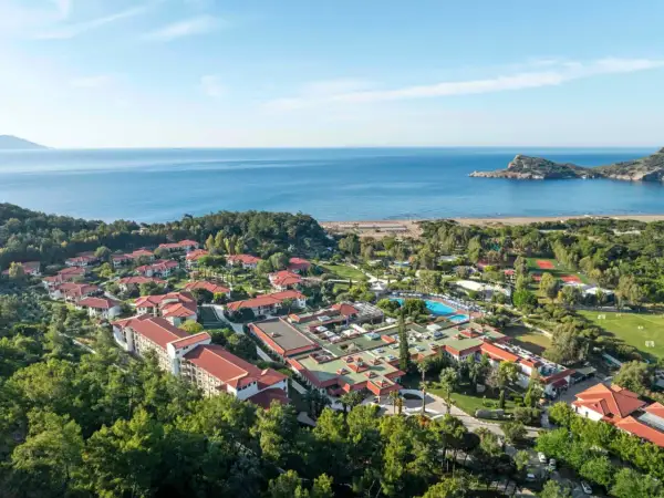 Luftaufnahme des TUI Blue Sarigerme Park mit Blick auf das Meer, Pools und Tennisplätze, eingebettet in üppige grüne Bäume.