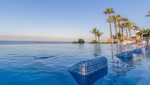 Infinity-Pool mit Blick auf das Meer und Palmen am Riu Palace Meloneras. Entspannung pur im blauen Wasser.