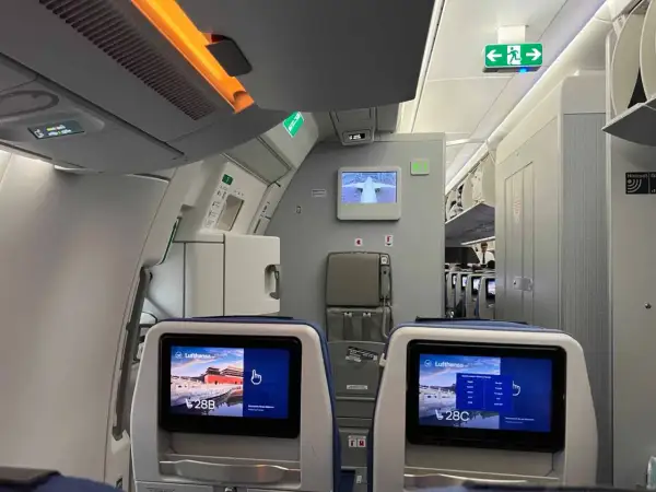 Blick in die Flugzeugkabine. Bildschirme zeigen "Lufthansa" und Sitzplatz 28B/C. Hier erfährst du, wo man im Flugzeug am besten sitzt.