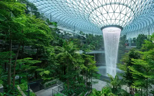 Imposanter Wasserfall im tropischen Garten des Flughafens Singapur. Die beeindruckende Architektur und üppige Vegetation lassen die **Singapur Flughafen Kosten** vergessen.
