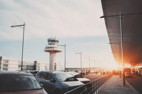 Autos parken am Flughafen Barcelona, mit dem markanten Kontrollturm im Hintergrund.