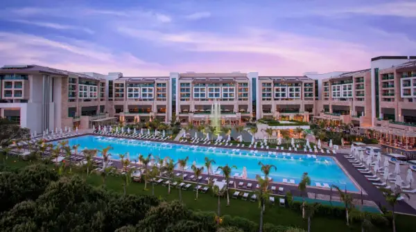 Ein luxuriöses Resort mit einem riesigen Pool und Palmen, das an das **Regnum Carya** erinnert. Abenddämmerung mit rosa Himmel.