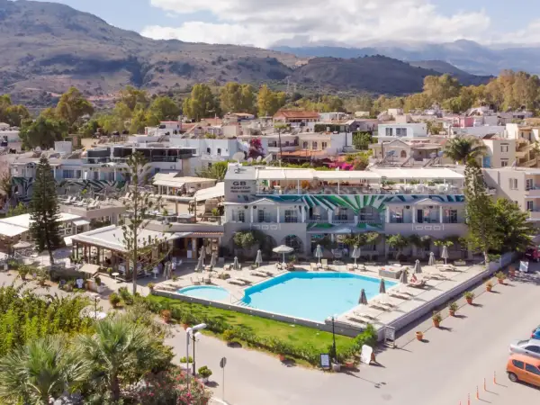 Ein **epos luxury beach hotel** mit Pool und Liegestühlen, umgeben von mediterraner Vegetation und Häusern, im Hintergrund Berge.