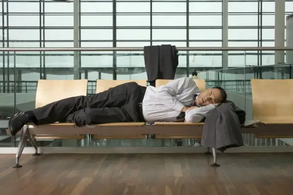 Mann schläft am flughafen auf einer Bank, sein Anzug hängt über der Lehne.