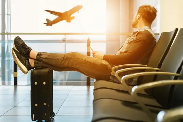 Mann mit Füßen auf Koffer wartet im Flughafen. Ein Flugzeug hebt ab.
