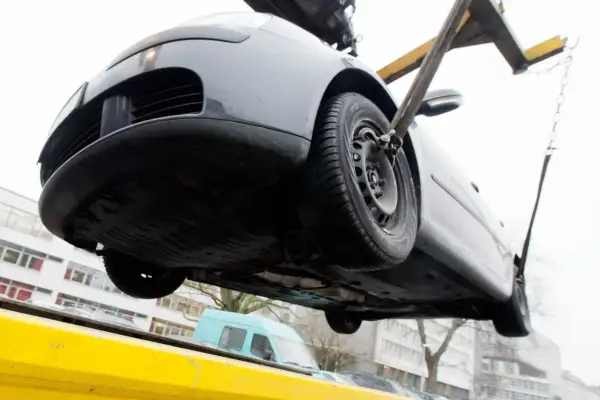 Ein graues Auto wird mit Gurten und Ketten von einem Abschleppwagen gehoben. Es muss wohl abgeschleppt werden.