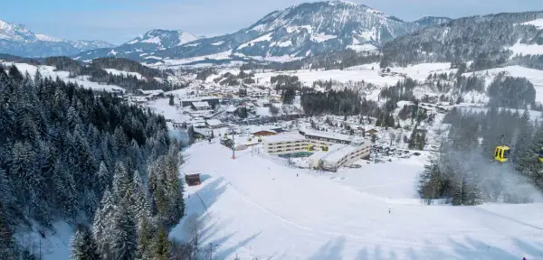 Winteridylle am Robinson Fieberbrunn: Hotelanlage mit Skilift und verschneiten Bergen im Hintergrund.