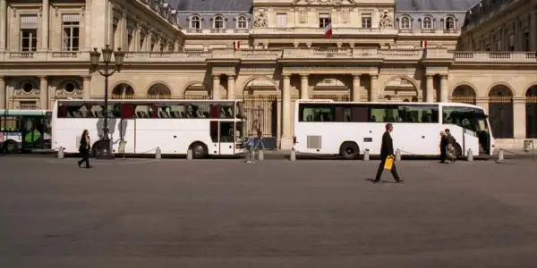 Weiße Reisebusse vor einem prächtigen Gebäude. Eine Frau geht vorbei. Wie kommt man am besten nach Paris? Mit dem Bus!