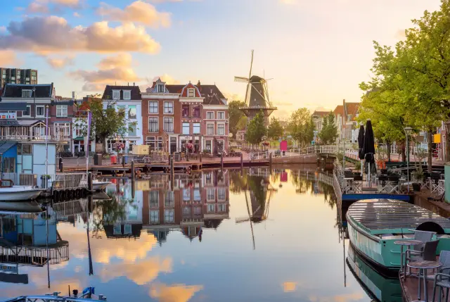 Ein malerischer Kanal in Leiden, Holland, mit traditionellen Häusern, einem Windrad und reflektierenden Wolken im Wasser.